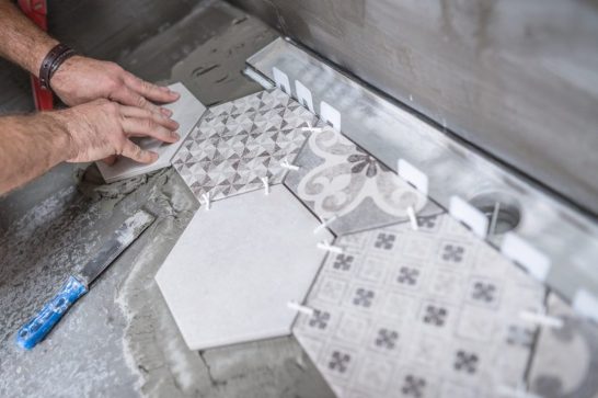 Anonymous image of male constructor aligning and pressing ceramic tile on the floor